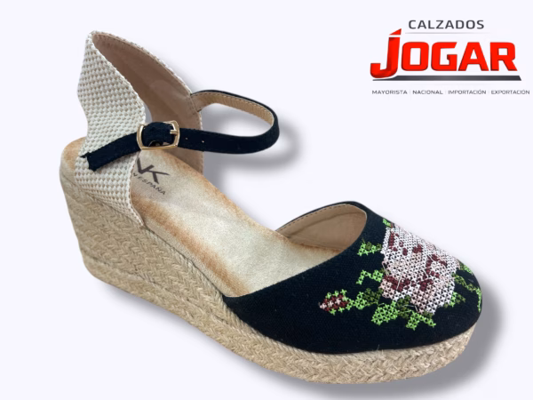 Alpargata de cuña media en yute natural con puntera cerrada de lona oscura decorada con un bordado floral multicolor en punto de cruz, talonera de tejido rústico y cierre de pulsera con hebilla.