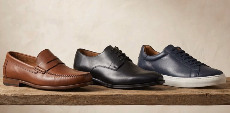 Tres estilos de calzado masculino en piel: mocasín clásico, zapato de cordones elegante y sneaker premium sobre estante de madera.